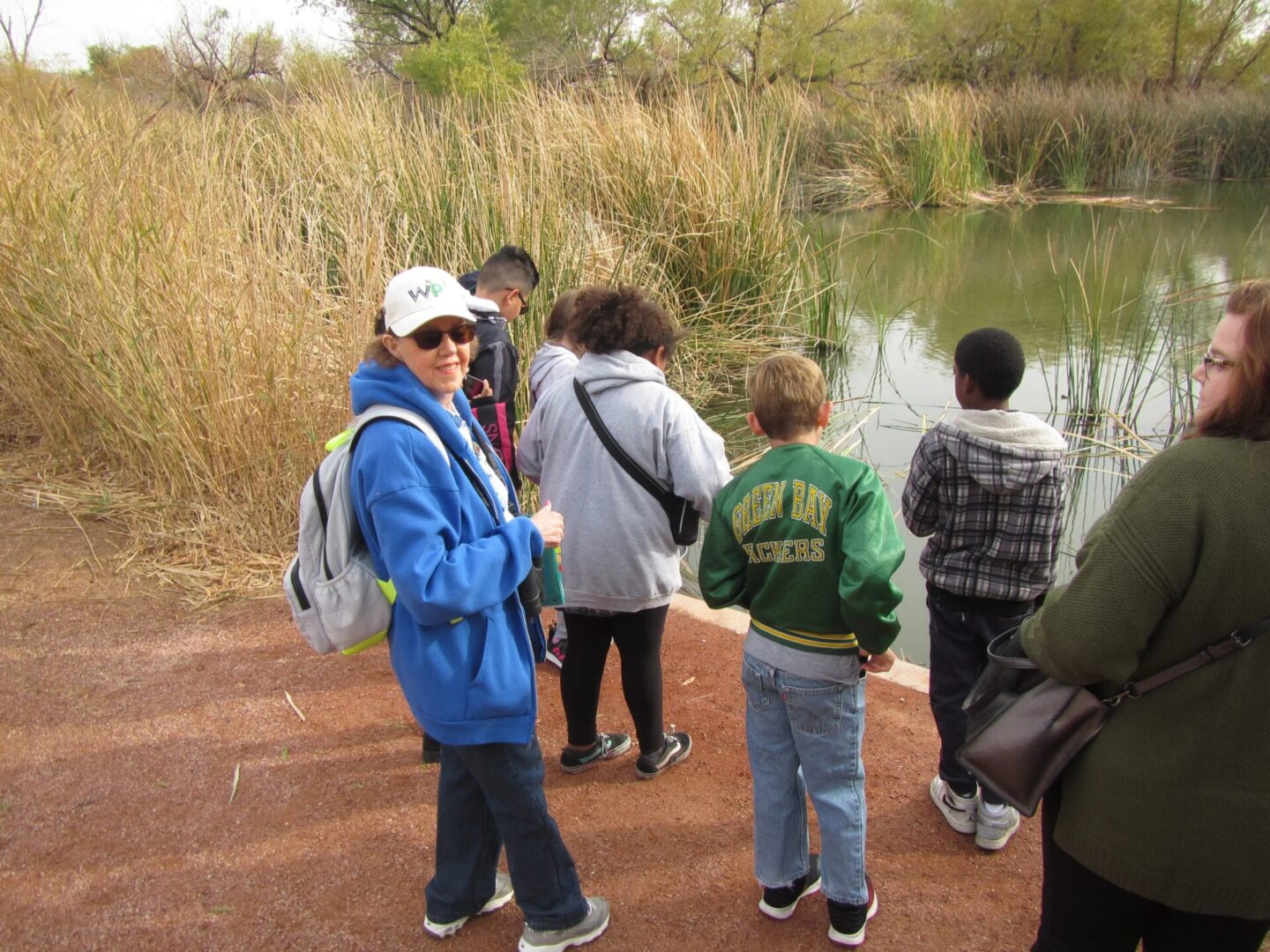 A group of people standing near a pond with reeds.