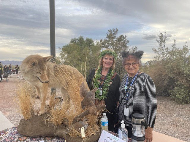 Two women standing in front of a table with a coyote.