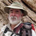 Man with white beard wearing a hat and backpack.