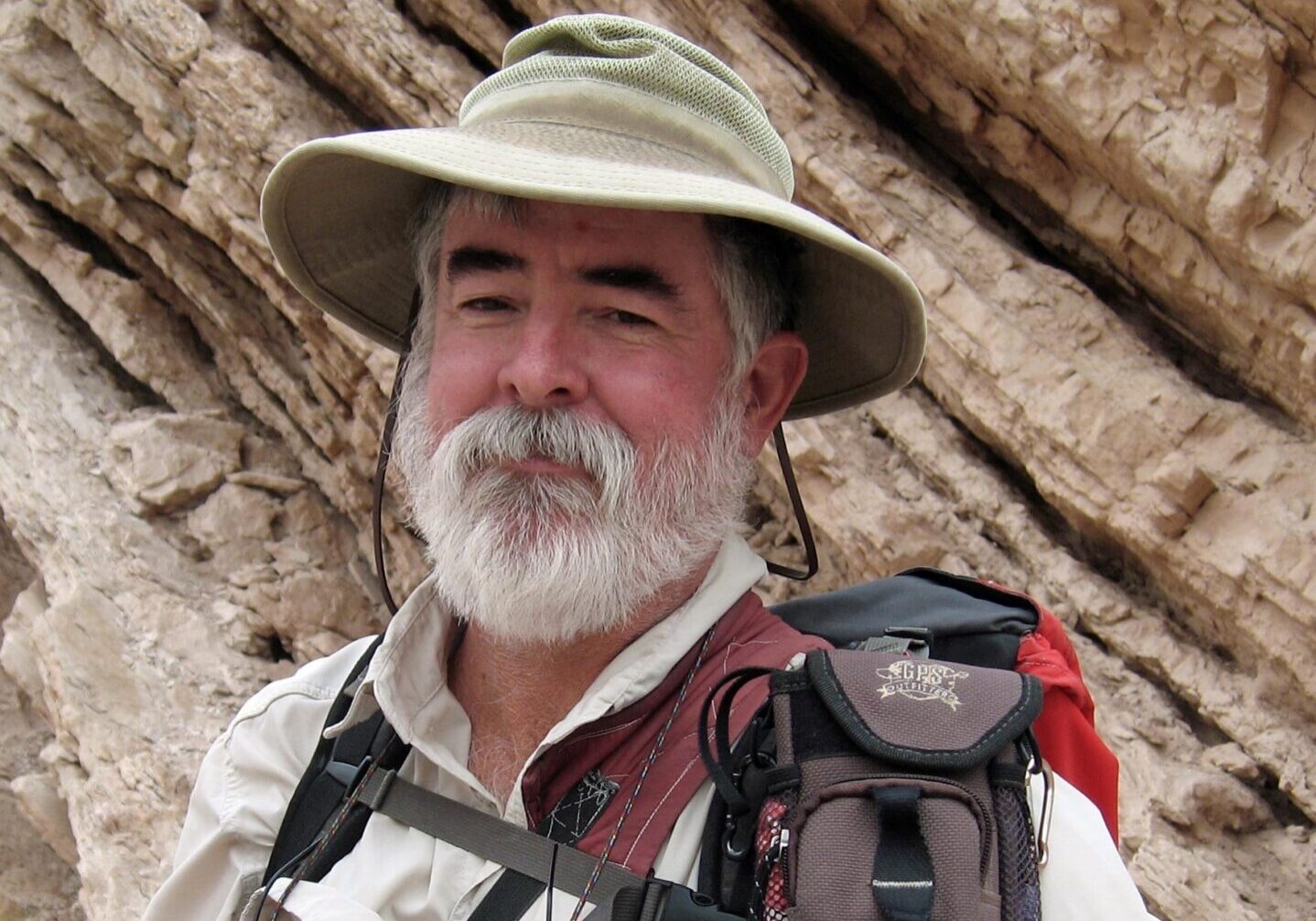 Man with white beard wearing a hat and backpack.