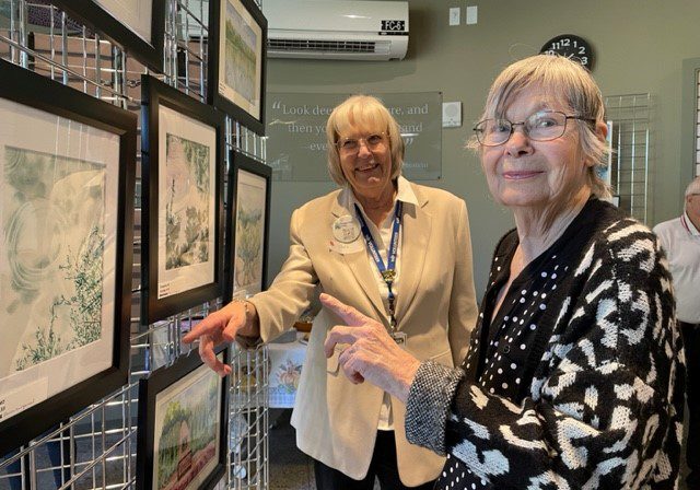 Two older women looking at framed artwork.